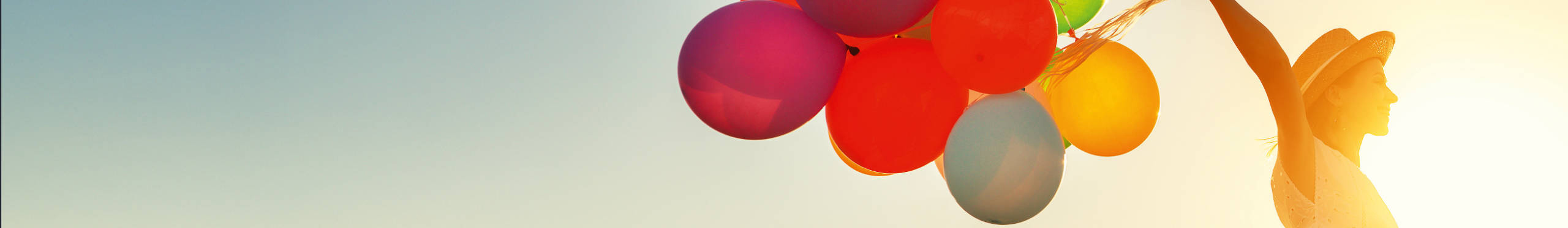 Eine Person im Sonnenlicht hält bunte Luftballons in der Hand. Der Himmel ist klar und blau. Die Szene vermittelt ein Gefühl von Freiheit und Freude.